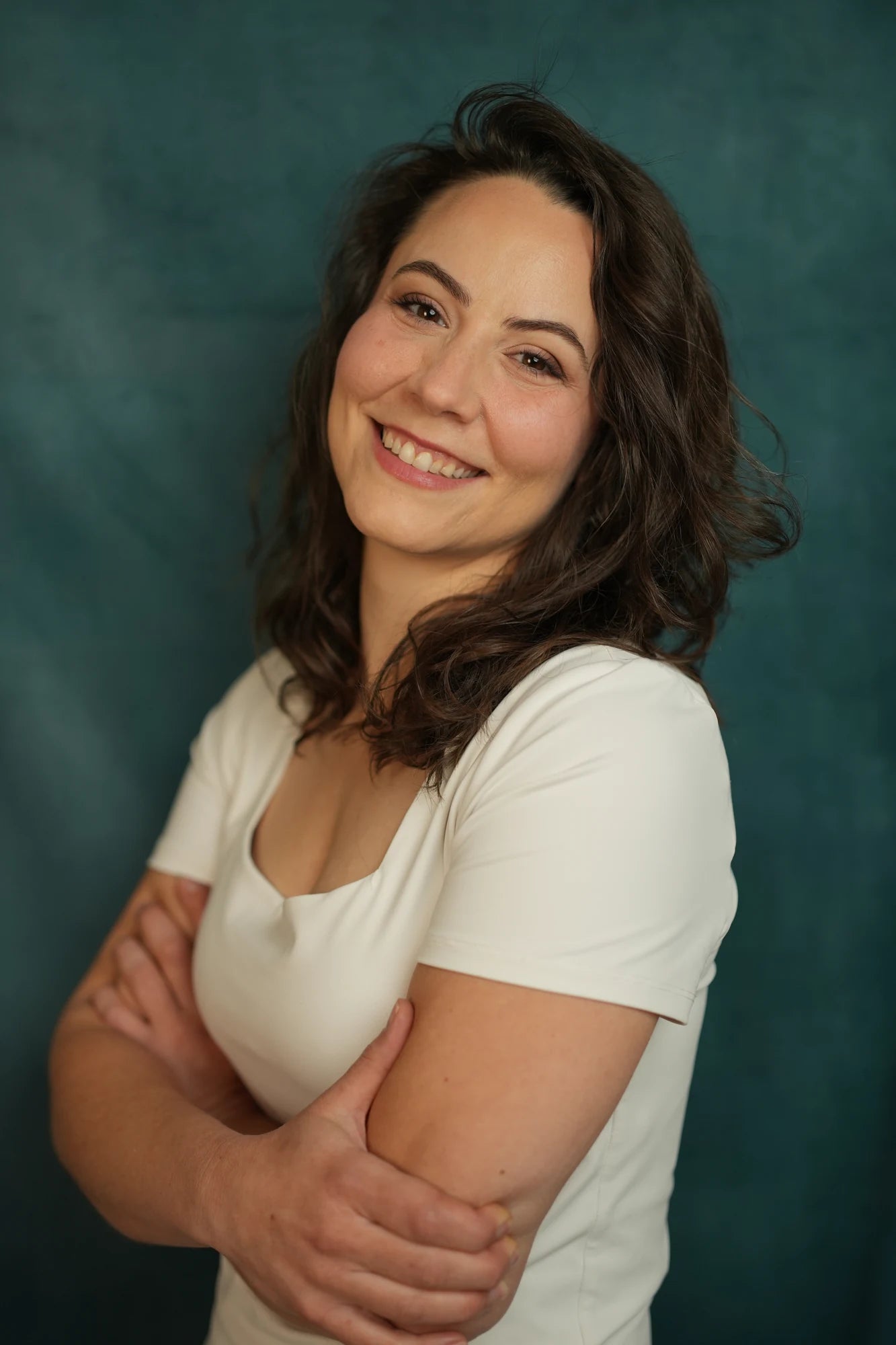 Maggie Baer smiling in a white top against a deep teal backdrop