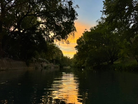 A sheltered river framed by trees, reflecting the gold of the evening sky.
